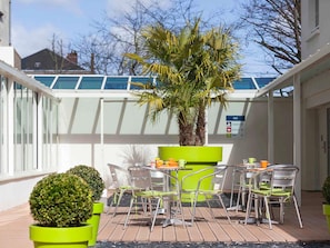 A patio with a table and chairs, a palm tree, and a sign indicating a reception area. - ibis Styles Saumur Gare Centre (Saumur)