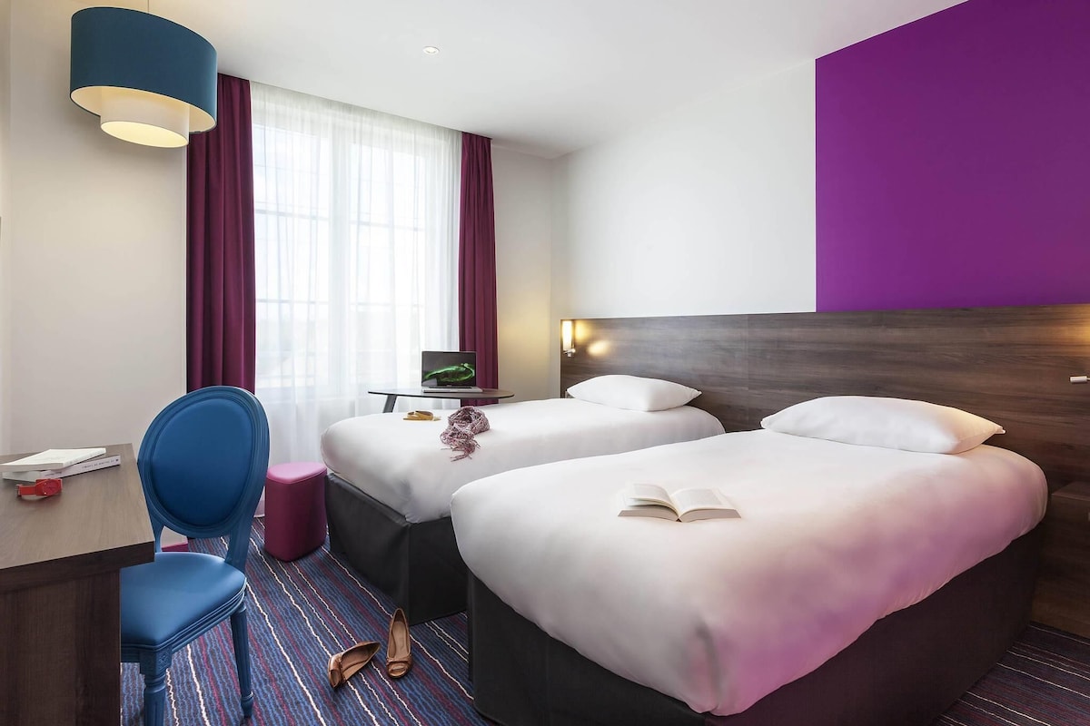 Habitación de hotel con dos camas, un escritorio, una silla, una computadora portátil y una ventana con cortinas.