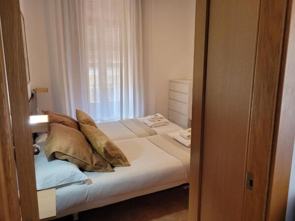 A bedroom with a bed, a bedside table, a dresser, and a window with curtains.