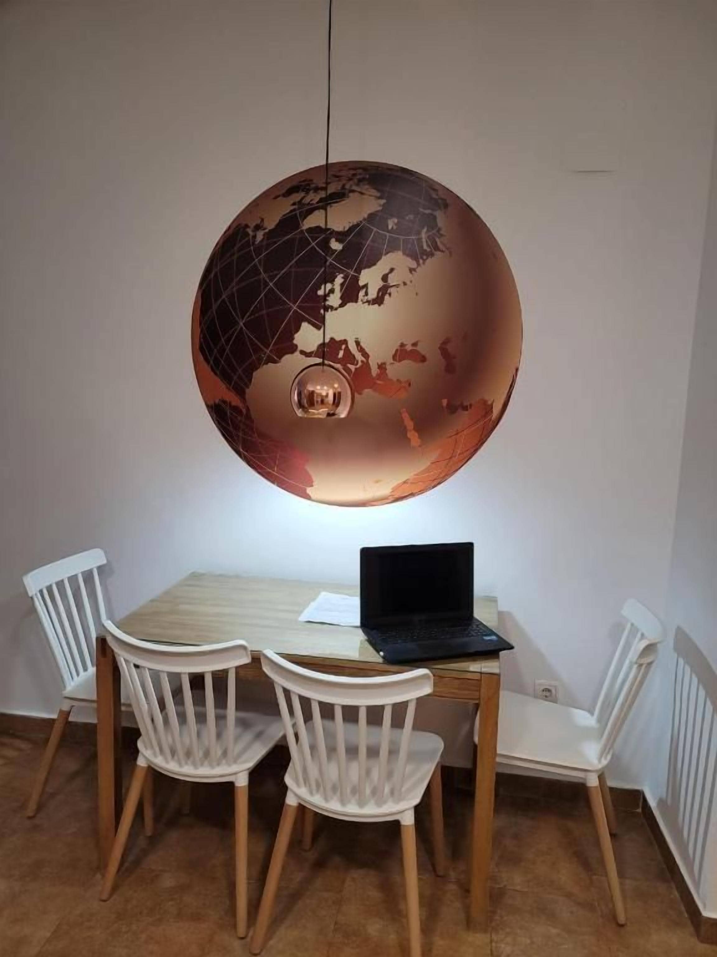 Un coin repas avec une table en bois, quatre chaises blanches et un luminaire en forme de globe.