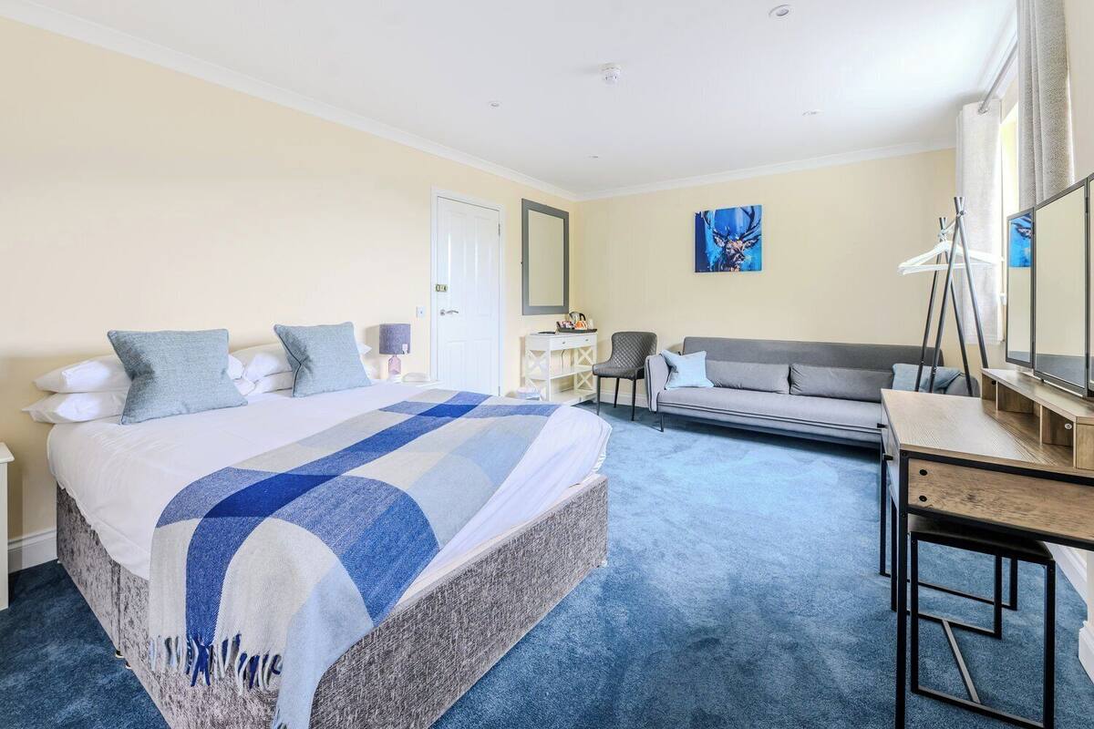 A hotel room with a large bed, a grey sofa, a desk, and a mirror.