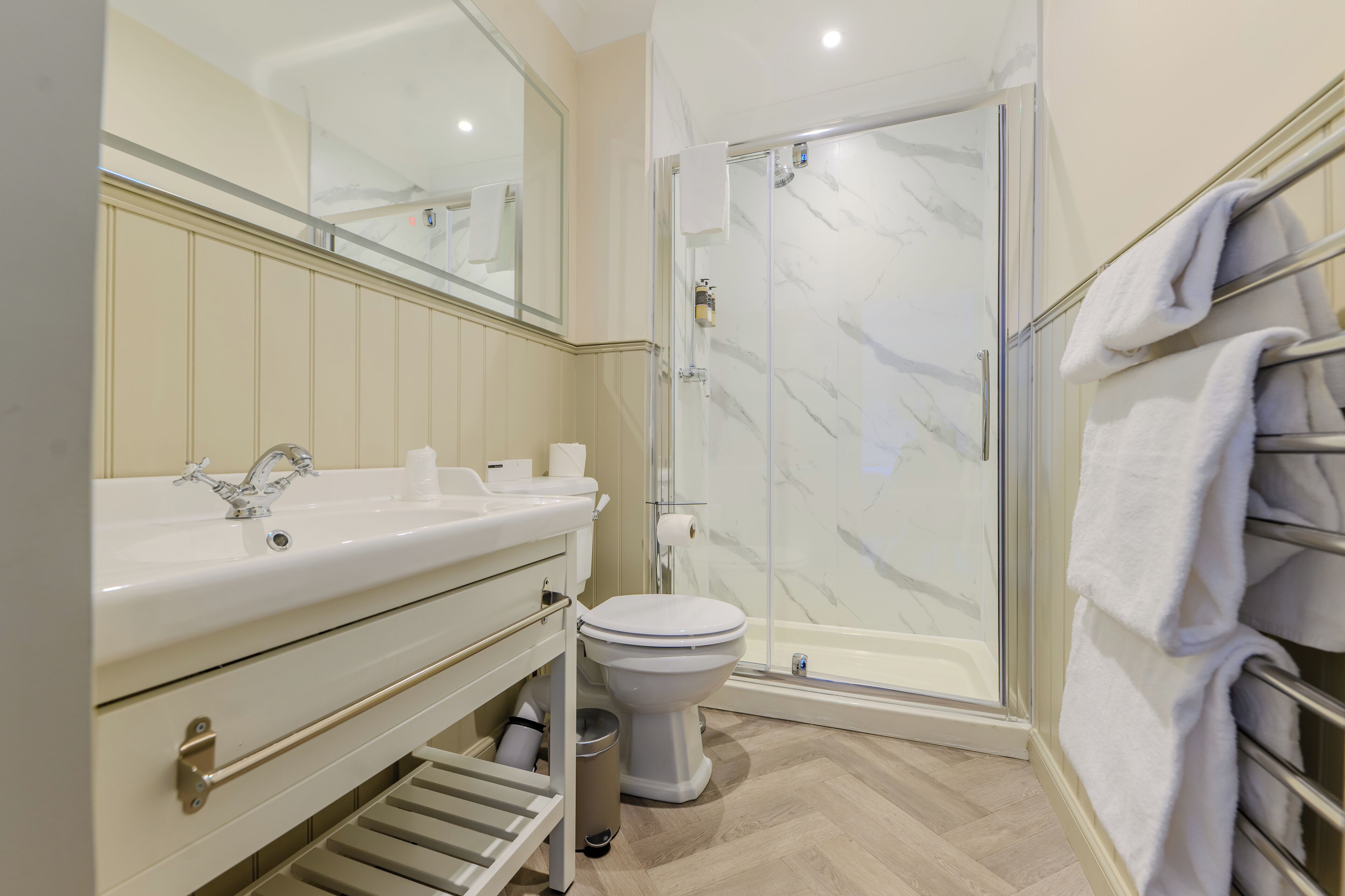 A modern bathroom with a glass-enclosed shower, a white sink with a mirror above, and a towel rack with folded towels.