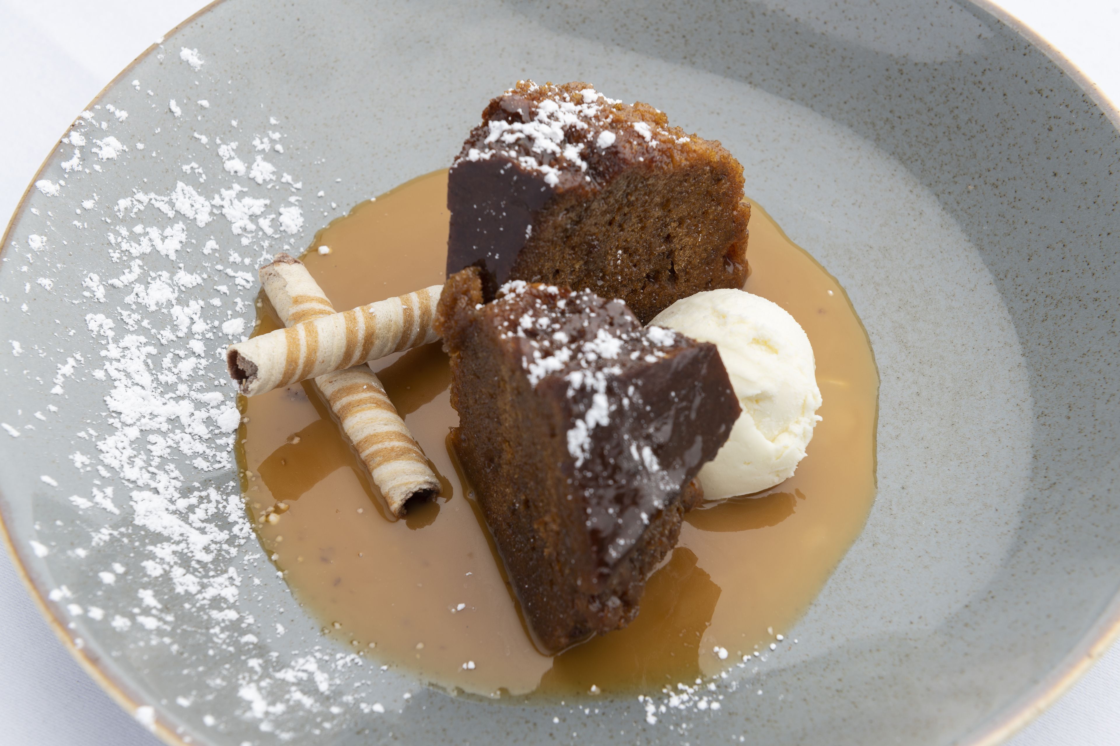 Un plato de postre con una porción de pastel, una bola de helado y un cono de gofre.