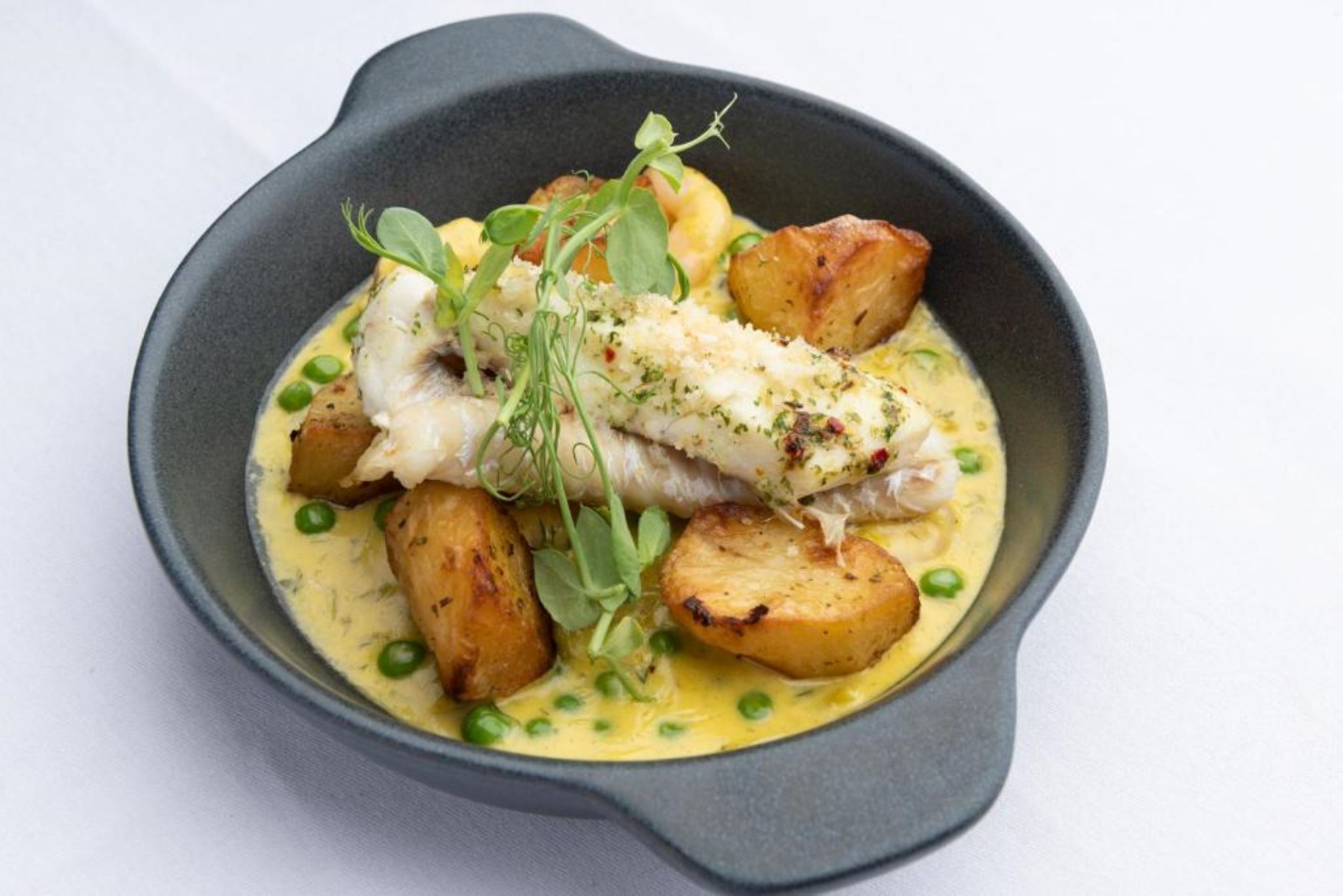 Un plat composé de poisson, de pommes de terre et de petits pois, servi dans un bol.