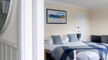 Un dormitorio con una cama, una mesita de noche, una lámpara, un cuadro enmarcado en la pared y una puerta.