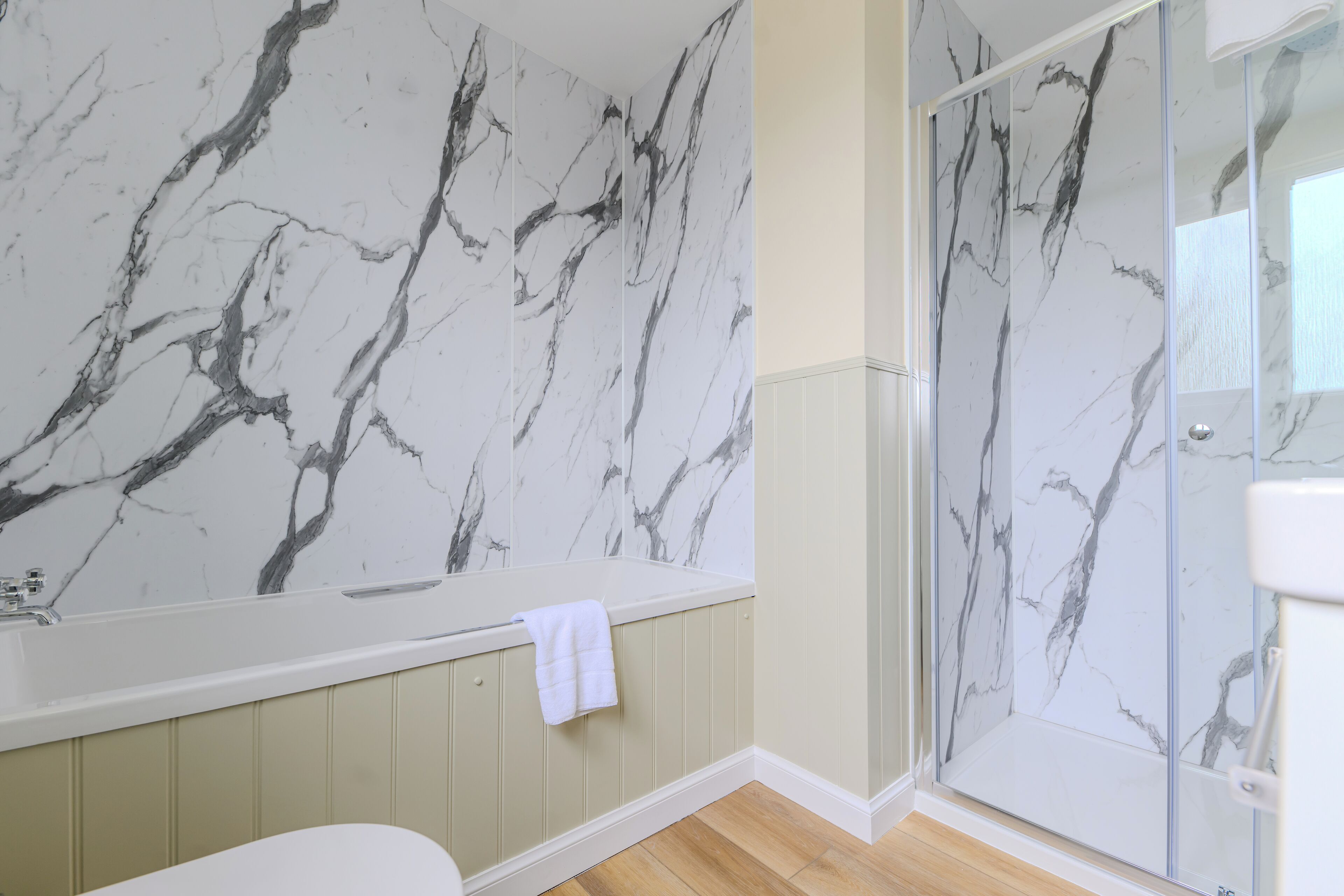 A bathroom with a marble wall, a bathtub, and a glass shower enclosure.