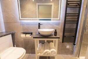 Un baño moderno con piso de mármol, lavamanos blanco, espejo y toallero.