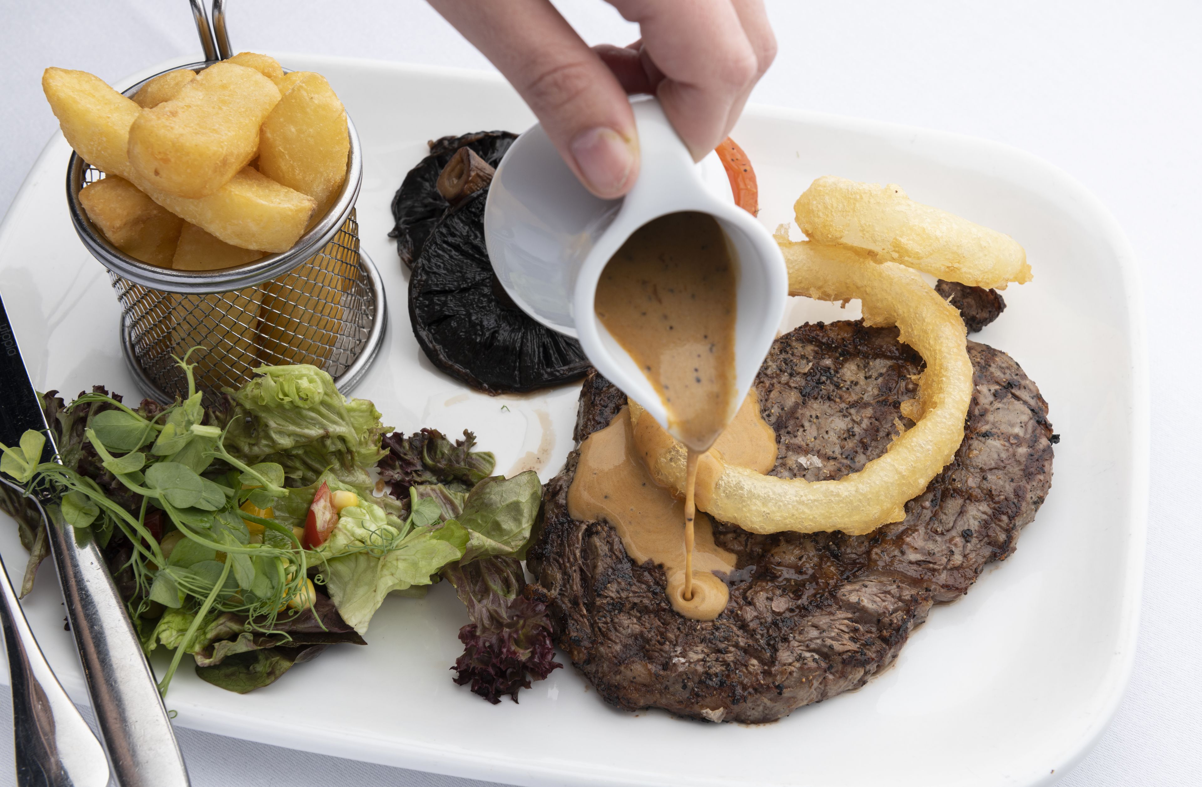 Un plato con un bistec, aros de cebolla y una ensalada.