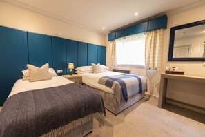 A bedroom with two beds, a nightstand, a dresser, and a large window with curtains. - Loch Ness Clansman Hotel (Inverness)