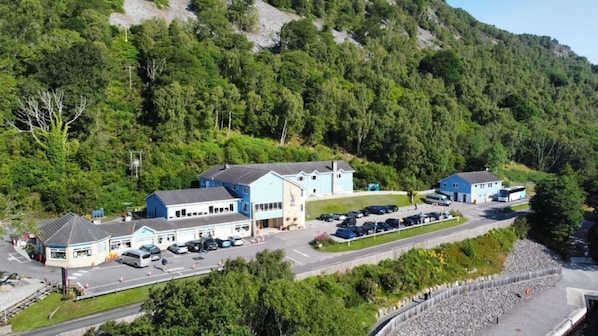 A building complex with multiple structures, a parking area, and a surrounding forested hillside. - Loch Ness Clansman Hotel (Inverness)