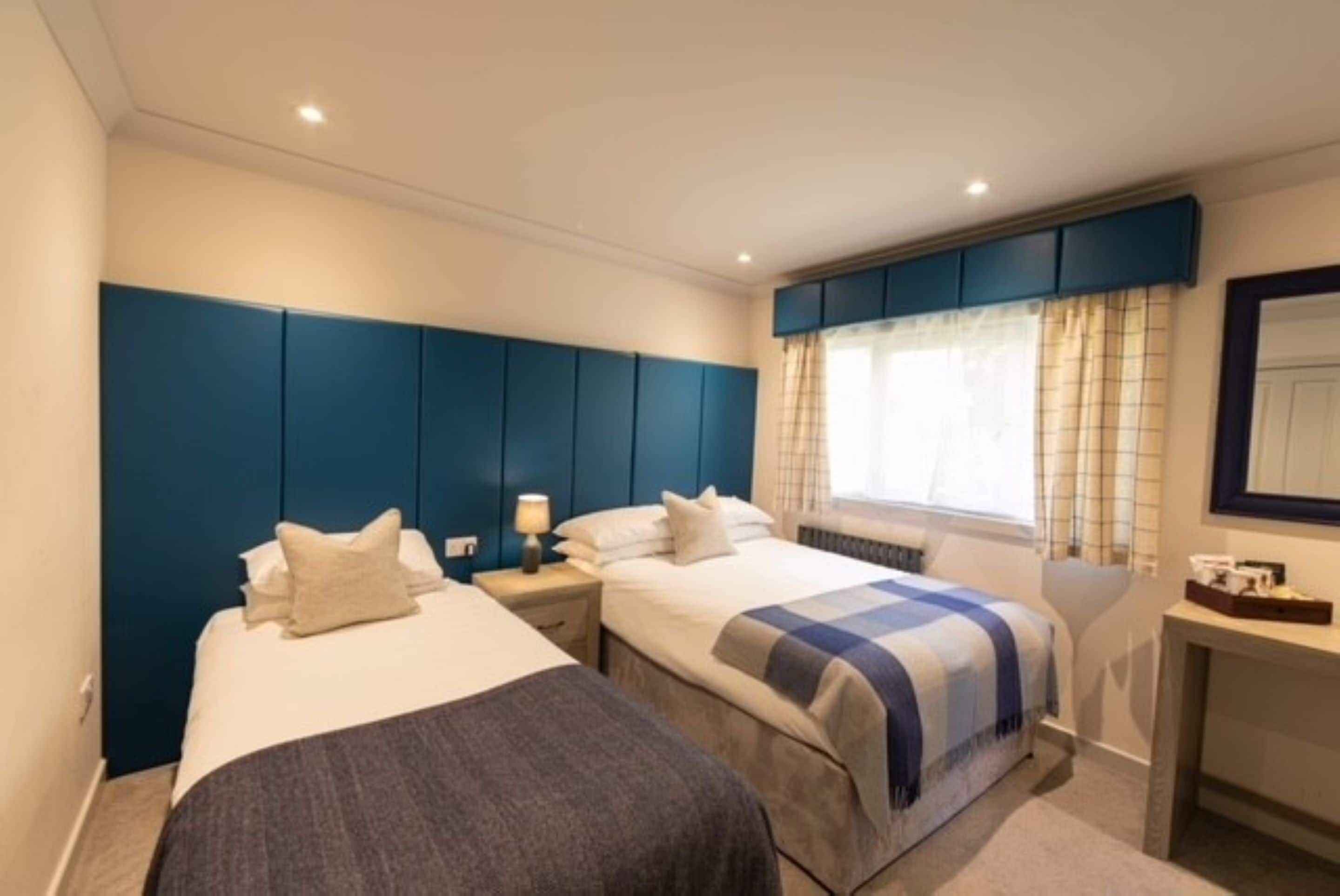 A hotel room with two beds, a desk, and a window with curtains.