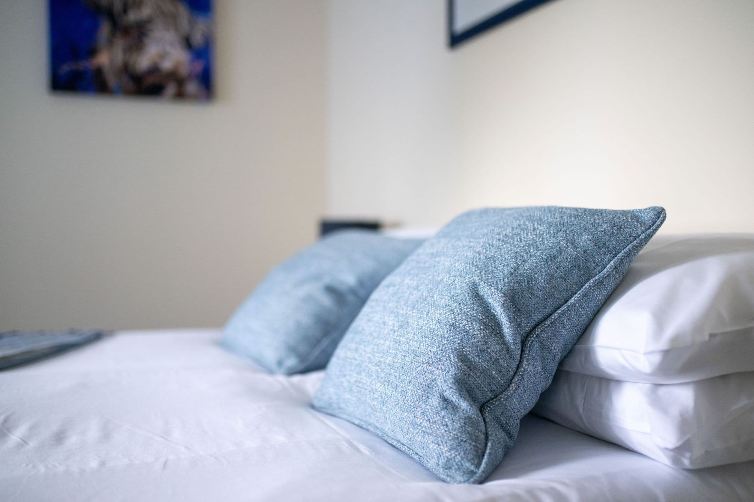A bed with white bedding and two light blue pillows.