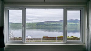 Una ventana con vista a un lago, un barco y colinas a lo lejos.