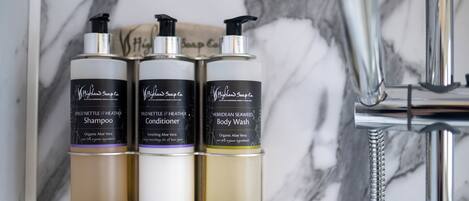 Tres botellas de champú, acondicionador y jabón de cuerpo Wild Nettle & Heather sobre una pared de mármol.