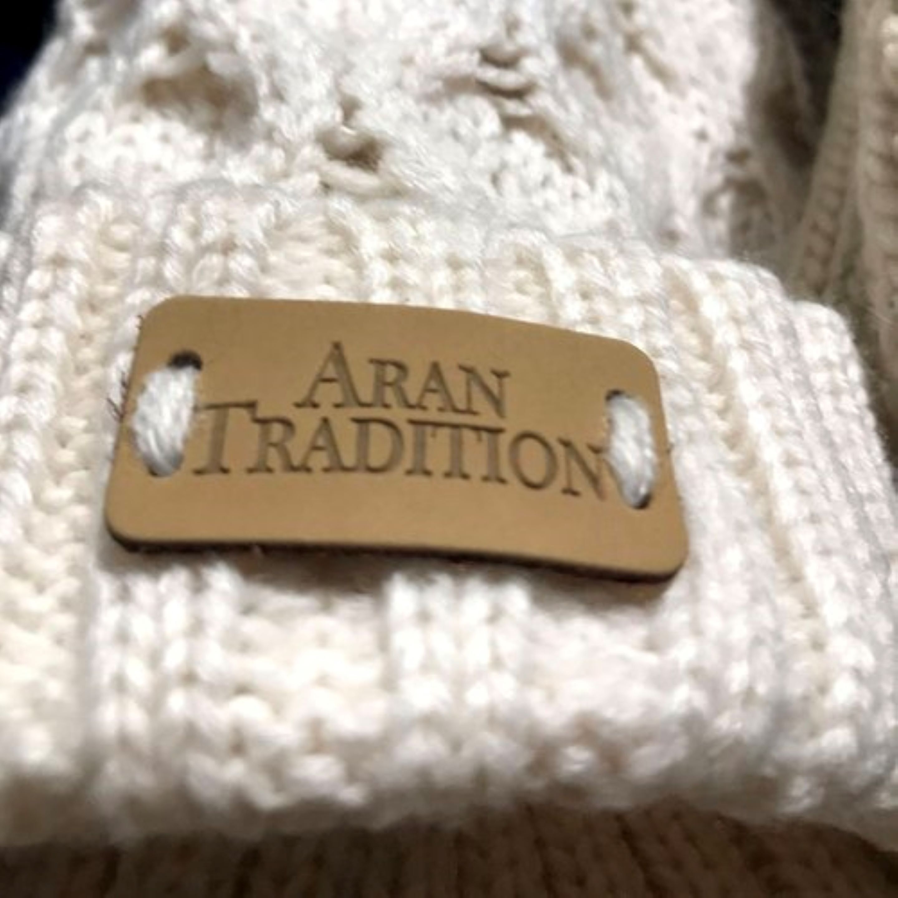 A tag with the text "ARAN TRADITION" on a knitted fabric background.