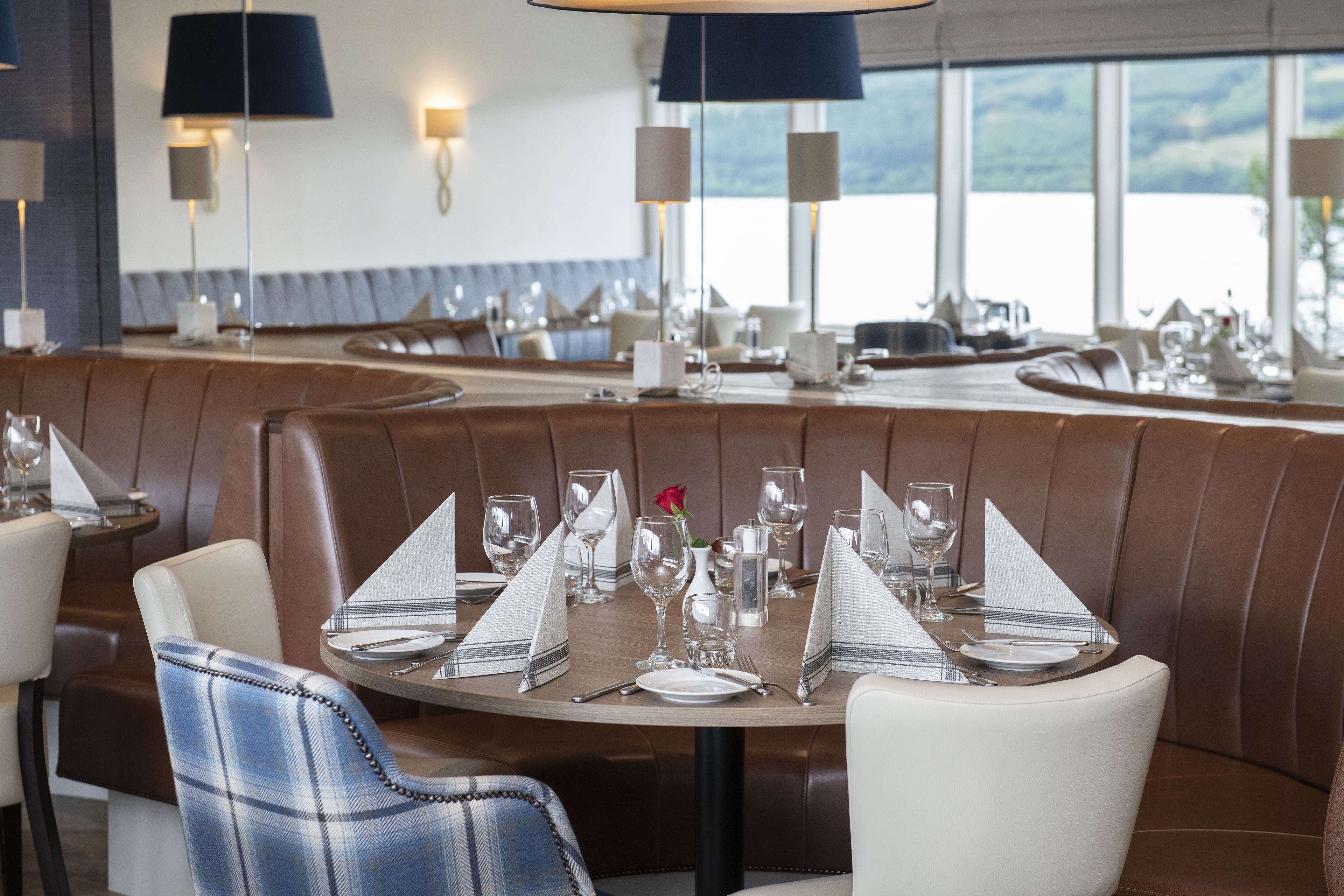 A restaurant with a booth seating area, round tables with set dining ware, and a view of the outdoors.