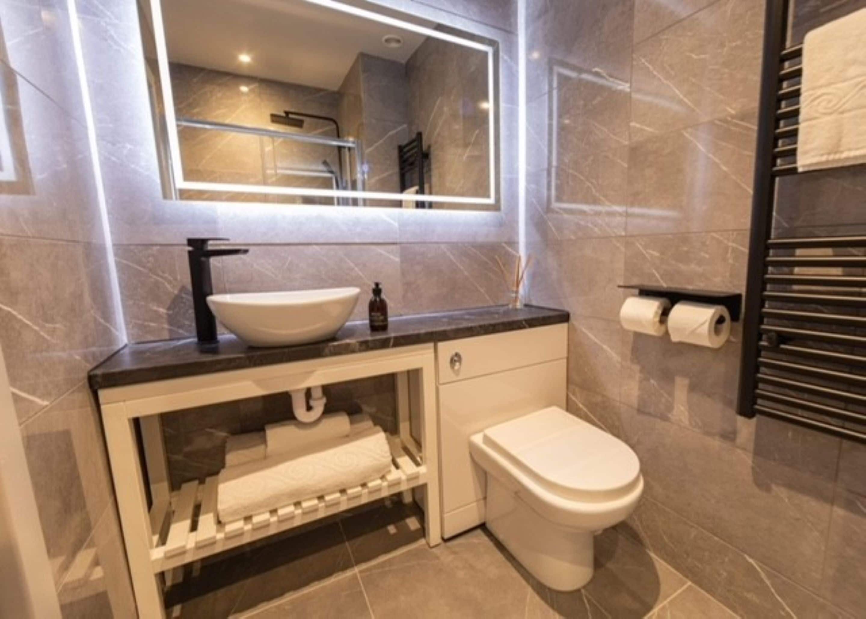 A modern bathroom with a large mirror, a white sink, a toilet, and a towel rack.