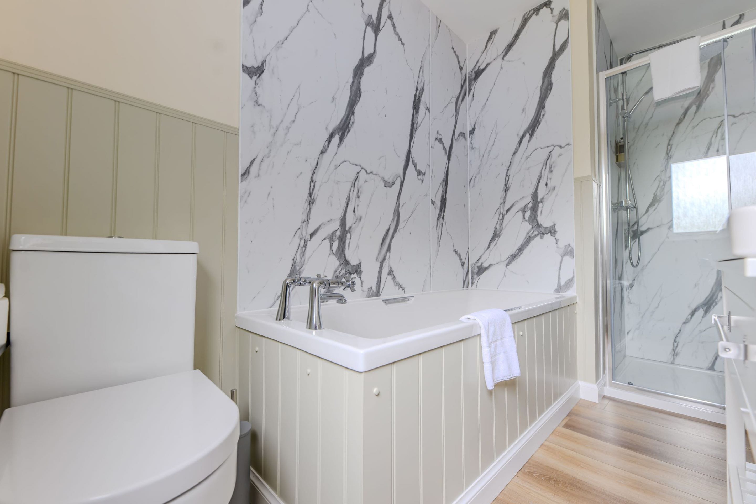 Een badkamer met toilet, een bad met marmeren wand en een douchecabine van glas.