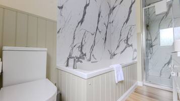 Een badkamer met toilet, een bad met marmeren wand en een douchecabine van glas.
