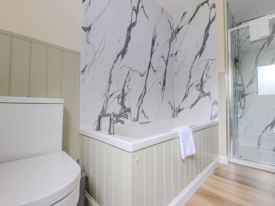 Een badkamer met toilet, een bad met marmeren wand en een douchecabine van glas.
