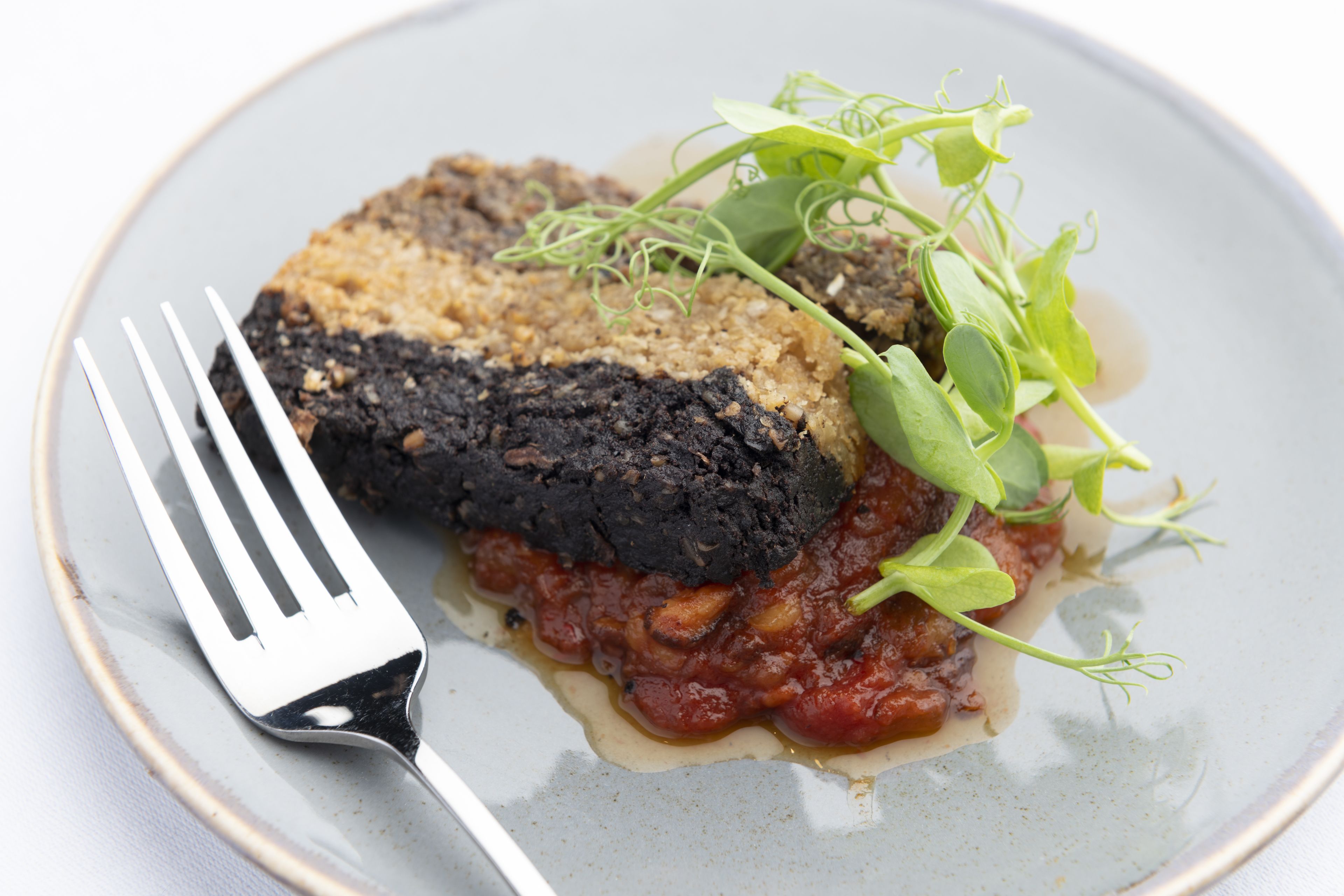 A plate with a charred piece of food, a fork, and some greens.