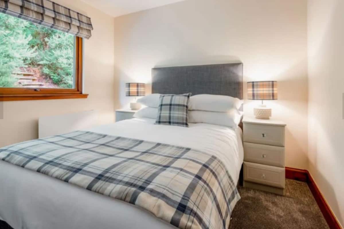 A neatly arranged bedroom with a large bed, two bedside tables, and a window with a view of greenery.