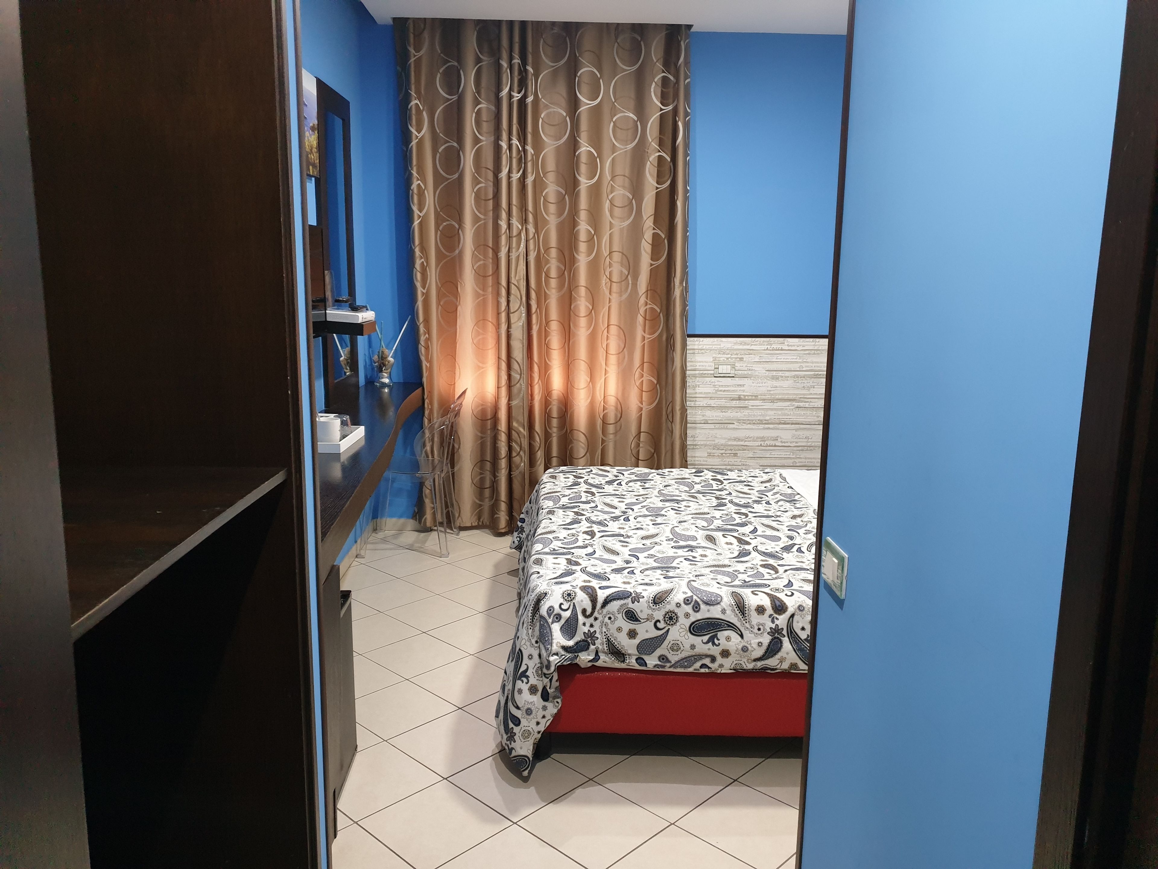 A small, compact bedroom with a bed, a nightstand, a mirror, and a curtain.