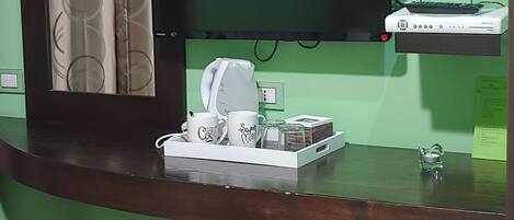 Quarto com escrivaninha de madeira, televisão de tela plana na parede, pequeno armário sob a escrivaninha e cortina com padrão circular.