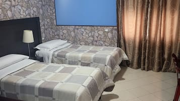 A hotel room with a stone wall, a painting of a cityscape, a bed with a checkered bedspread, and a curtain with a circular pattern.