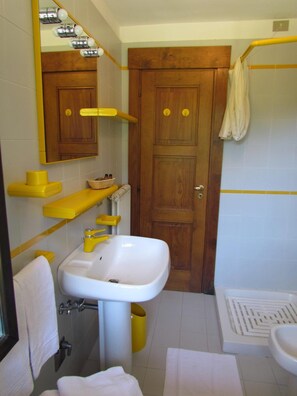 A bathroom with a white sink, yellow towel holders, a wooden door, and a shower area. - Il Piccolo Residence (Gressoney-la-Trinite)