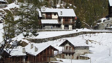 A snow-covered mountain lodge with multiple wooden buildings, stone walls, and a ski slope.