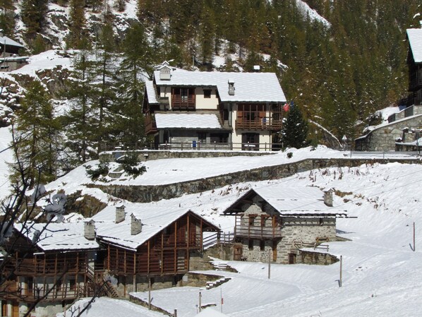 A snow-covered mountain lodge with multiple wooden buildings, stone walls, and a ski slope. - Il Piccolo Residence (Gressoney-la-Trinite)