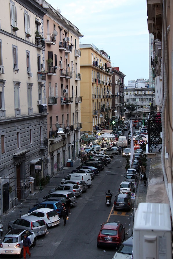 Un carrer estret flanquejat per edificis d'alguns pisos, cotxes aparcats i alguns vianants.