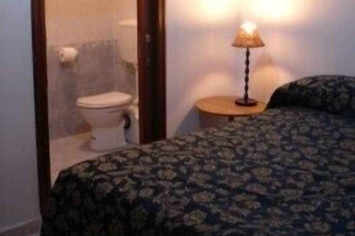 A room with a bed, a nightstand, a lamp, and a door leading to a bathroom.