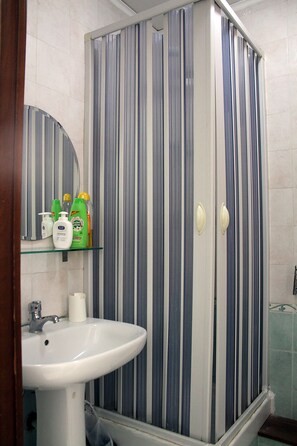 A bathroom with a striped shower enclosure, a sink, and toiletries on a shelf. - B&B Cinquestelle (Naples)