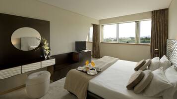 A hotel room with a large bed, a bedside table with a flat-screen TV, a round mirror, and a view of the outdoors through the window.