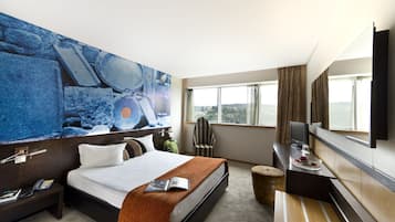 Et hotelværelse med en stor seng, et skrivebord med et fladskærms-tv, en stol og et vindue med udsigt over byen.