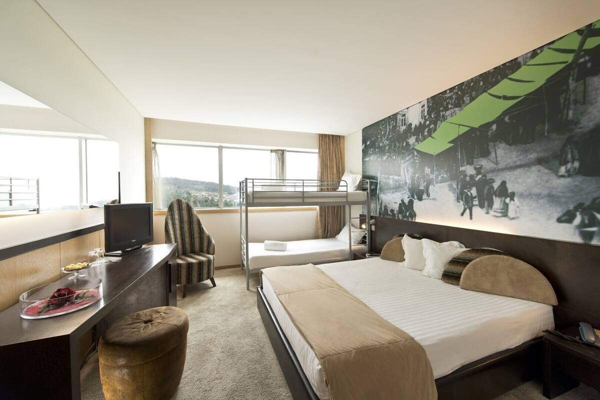 Une chambre d’hôtel avec un lit superposé, un bureau avec un ordinateur, une chaise et une grande fenêtre.