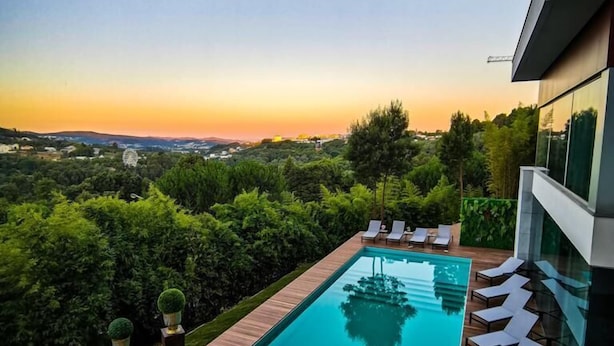 A modern outdoor pool area with a wooden deck, lounge chairs, and a view of the landscape. - Penafiel Park Hotel & Spa (Penafiel)