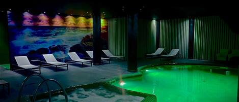 Un espace de bien-être comprenant une piscine, des chaises longues et une fresque représentant une scène de plage.