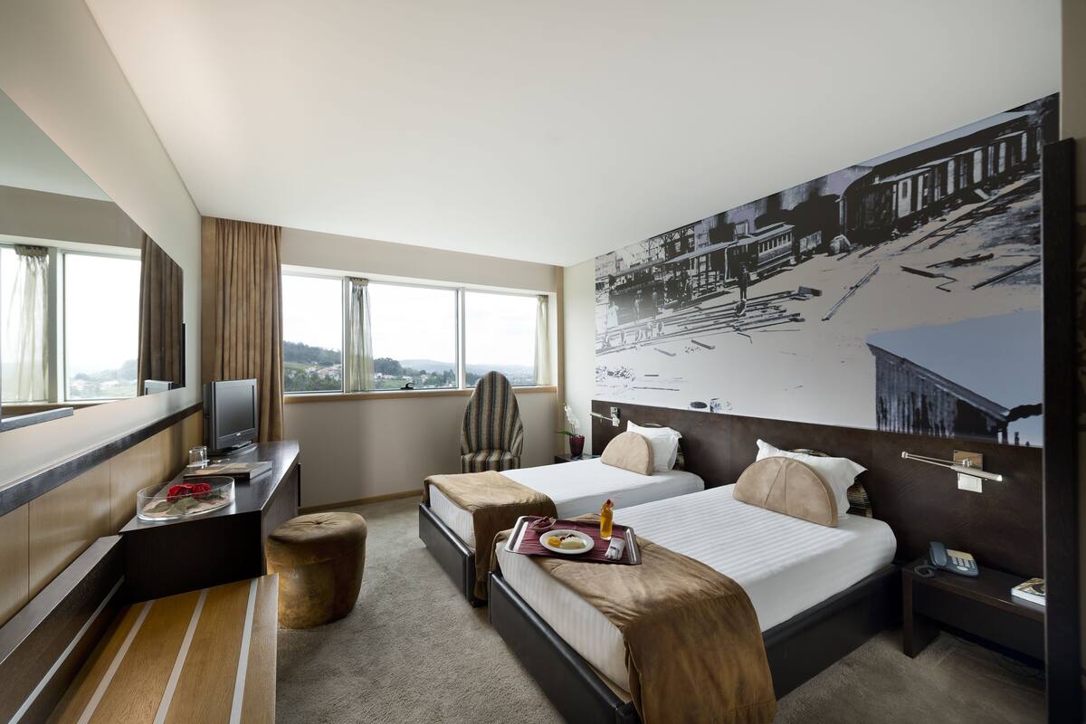 Une chambre d’hôtel avec deux lits, un bureau avec un ordinateur, une télévision et une grande fenêtre.