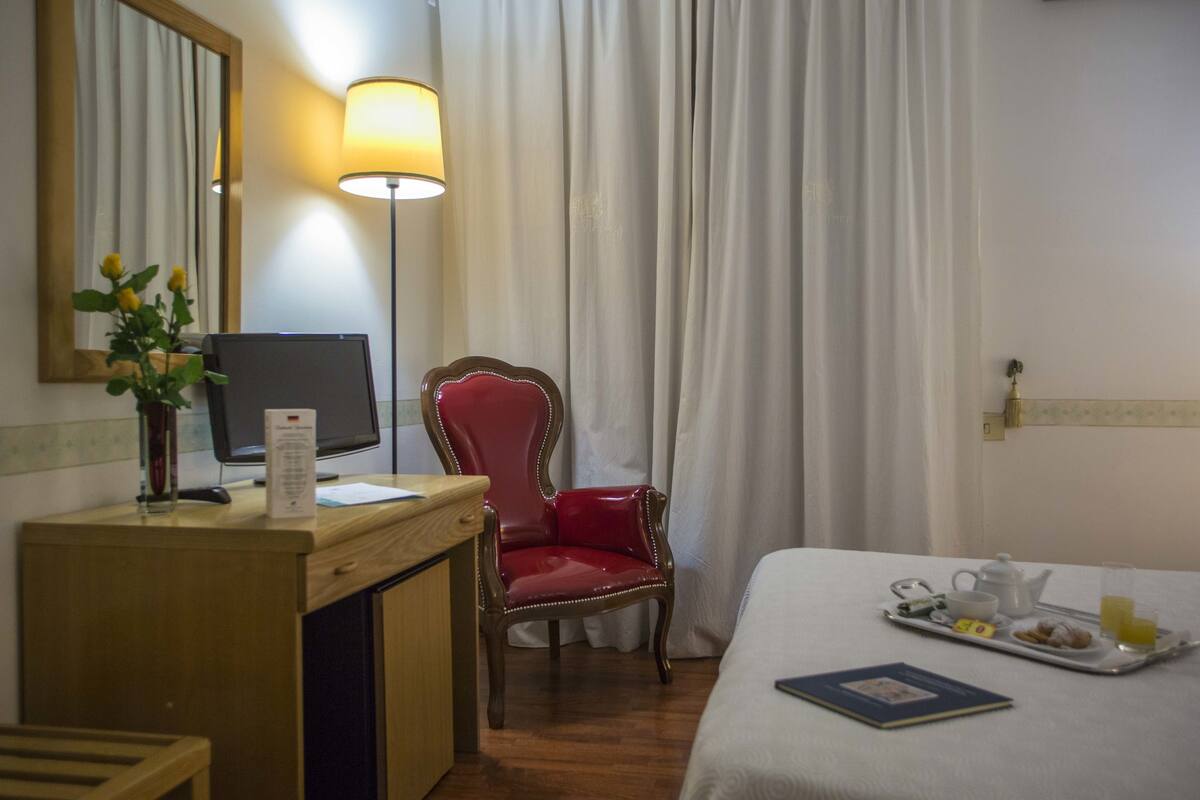 Ein Hotelzimmer mit Schreibtisch, einem roten Sessel, einem Bett und einem Tablett mit Frühstücksgegenständen.