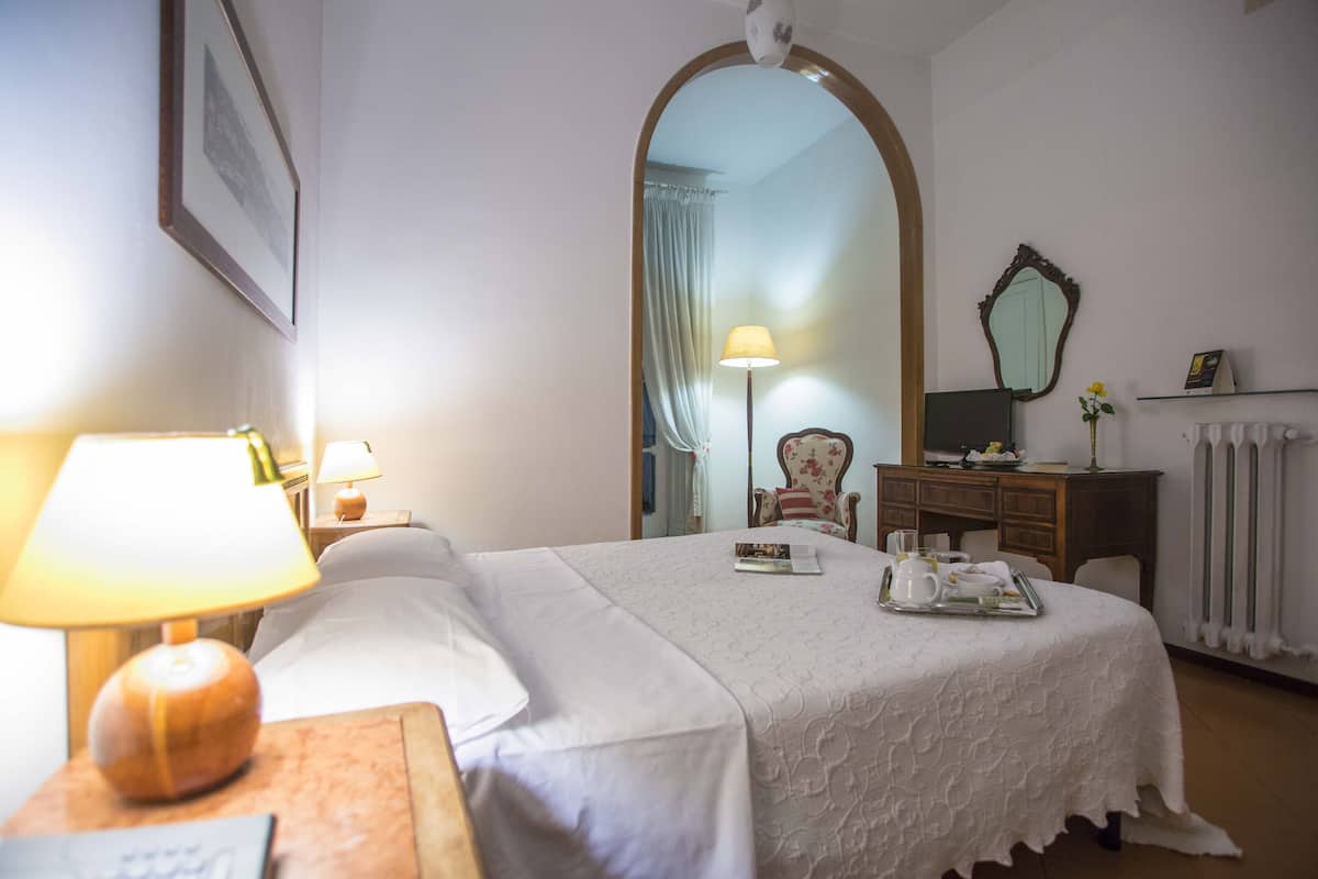 Ein Hotelzimmer mit Bett, Nachttisch mit Lampe, Kommode, Spiegel und Radiator.