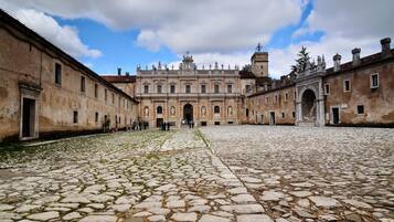 Une cour dallée de pierres, un grand bâtiment doté d’arcades et un ciel dégagé.