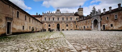 A courtyard with cobblestone flooring, a large building with arched doorways, and a clear sky.