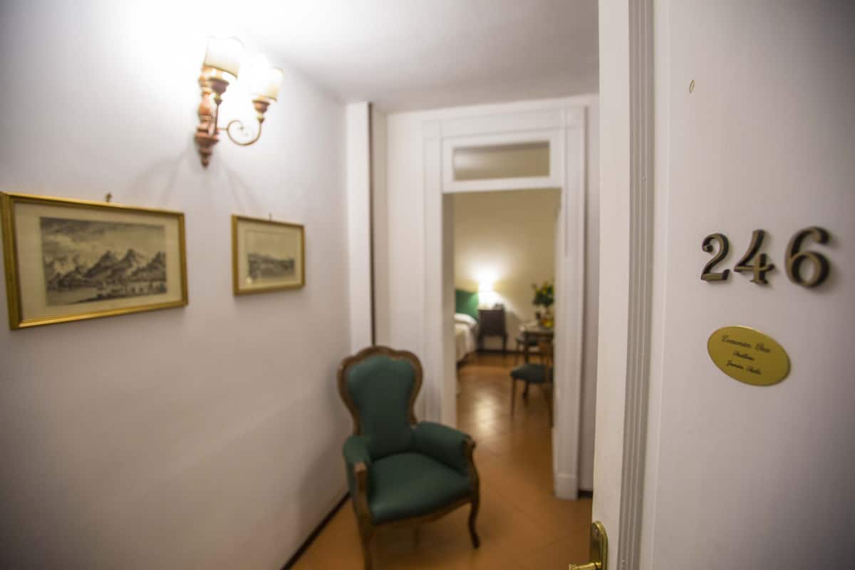 Ein Flur mit einem grünen Sessel, gerahmten Bildern an der Wand und einer Tür mit der Nummer 246.
