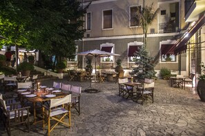 An outdoor dining area with tables and chairs, surrounded by potted plants and a stone floor. - Hotel Victoria Maiorino (Cava de' Tirreni)