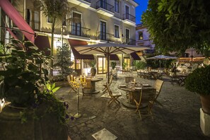 An outdoor café area with tables and chairs, surrounded by potted plants and a building with balconies. - Hotel Victoria Maiorino (Cava de' Tirreni)