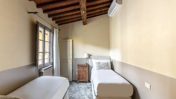 A room with two single beds, a wooden ceiling, an air conditioning unit, a small wooden cabinet, and a window with curtains.
