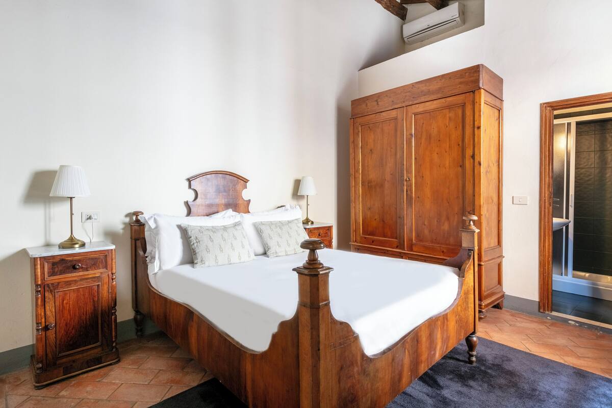 Un dormitorio con cama de madera, dos mesitas de noche con lámparas, un armario y la puerta del baño.